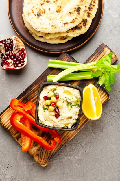 Vue plate sur un plat de houmous aux légumes garni de pois chiches et d'huile d'olive servi avec pita