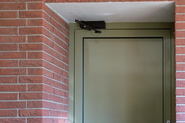 Vue de la porte fermée de la sortie d'évacuation du bâtiment lors d'un incendie ou d'un autre cataclysme Porte métallique avec un mécanisme d'ouverture moderne sur le fond d'un mur de briques Sortie de secours d'urgence