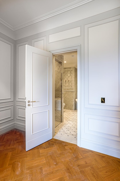 vue sur la porte ouverte sur la salle de bains en marbre design d'intérieur de luxe avec murs lambrissés blancs et parquet fl