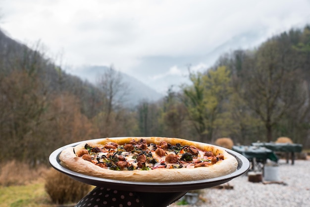 Vue à la première personne d'une main tenant une pizza dans un lieu naturel avec les montagnes de Slovénie