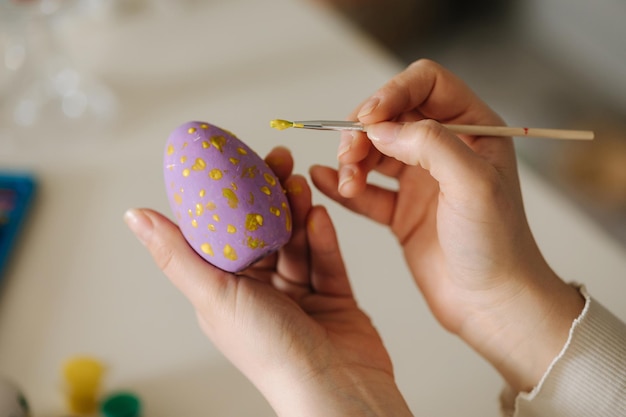 Vue à la première personne pf femme peignant des oeufs de pâques à l'aide d'un pinceau et de la peinture jaune vacances de printemps