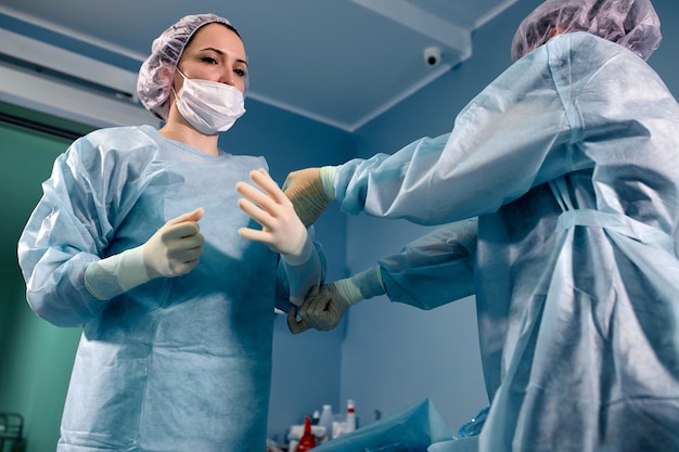 Vue de profil d'un assistant médical aidant un chirurgien à mettre ses gants dans une salle d'opération.