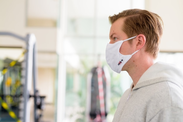 Vue de profil gros plan du jeune homme portant un masque à la salle de sport pendant la pandémie de virus corona covid-19