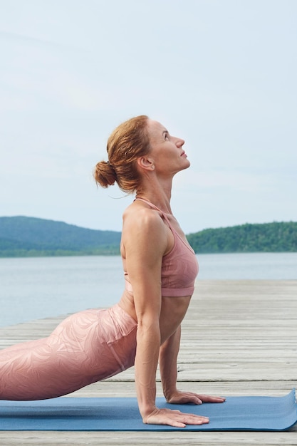 Vue de profil en gros plan d'une femme mûre en tenue de sport rose pratiquant le yoga