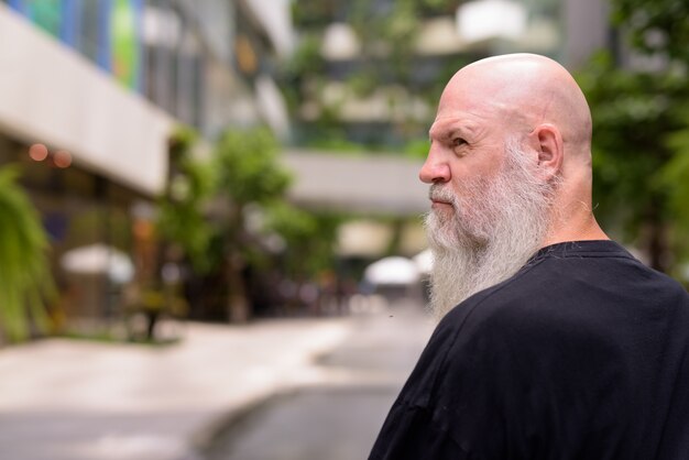 Vue de profil de l'homme barbu chauve mature avec la nature dans la ville