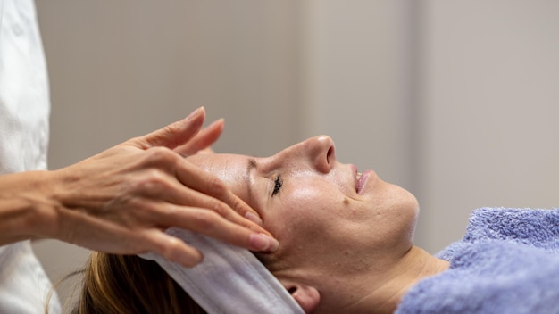 Photo vue de profil d'une jeune femme sur une table de massage recevant un soin du visage relaxant et rajeunissant