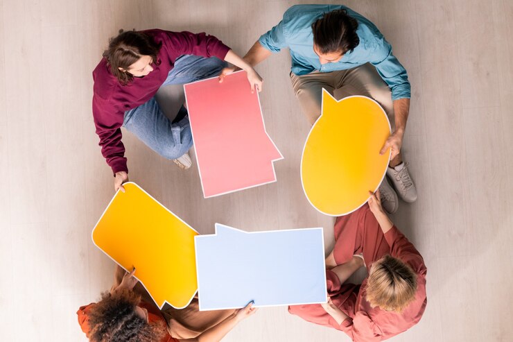 Vue de quatre jeunes concepteurs Web amicaux en vêtements décontractés, choisissant la forme de bulle de dialogue pour les réseaux sociaux ou les sites Web des clients