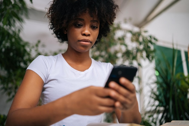 Vue rapprochée en angle bas d'une jeune femme africaine sérieuse tenant un téléphone portable dans les mains profitant de la navigation sur le Web communiquant sur le réseau social dans la chambre