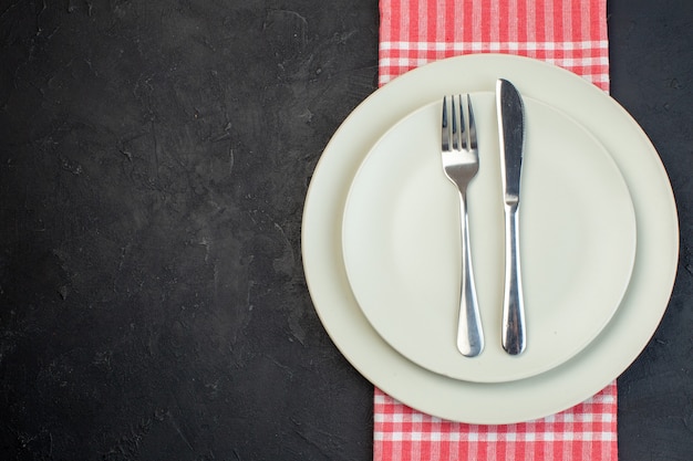 Vue rapprochée des assiettes vides blanches sur une serviette à rayures rouges et des couverts en acier inoxydable sur le côté gauche sur fond noir avec espace libre