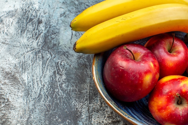 Vue rapprochée avant pommes rouges fraîches avec des bananes à l'intérieur du plateau sur fond sombre fruit mûr arbre photo fraîcheur du bois couleur du jus