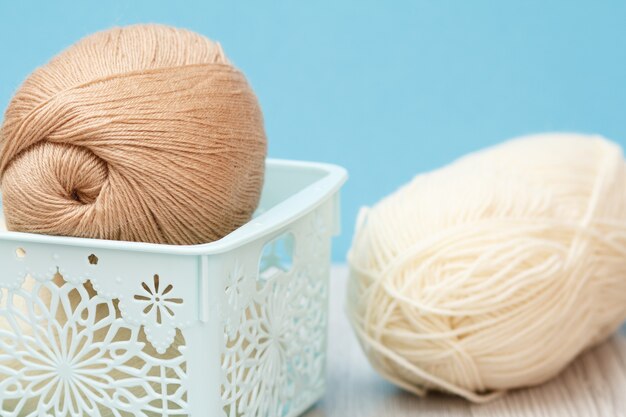 Vue rapprochée des boules de fil à tricoter dans un panier en plastique avec fond bleu. Notion de tricot. Faible profondeur de champ.