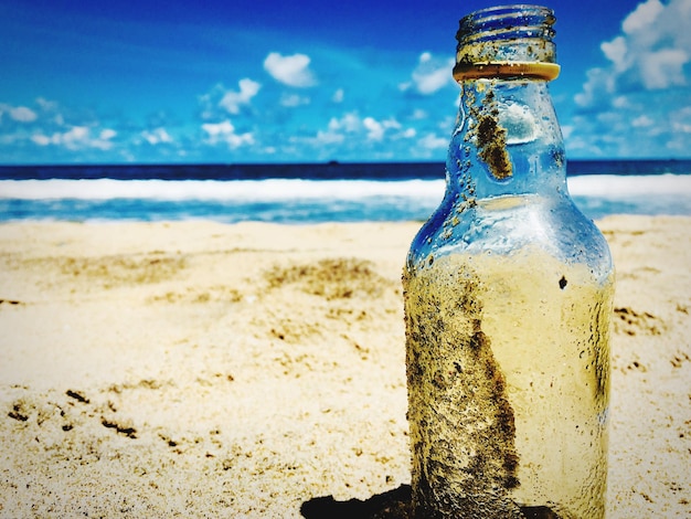 Vue rapprochée d'une bouteille de verre sur le sable de la plage contre le ciel