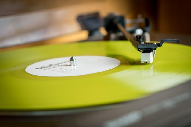 Vue rapprochée d'un bras de lecture et d'une platine jouant un disque vinyle couleur jaune Divertissement et tendances musicales