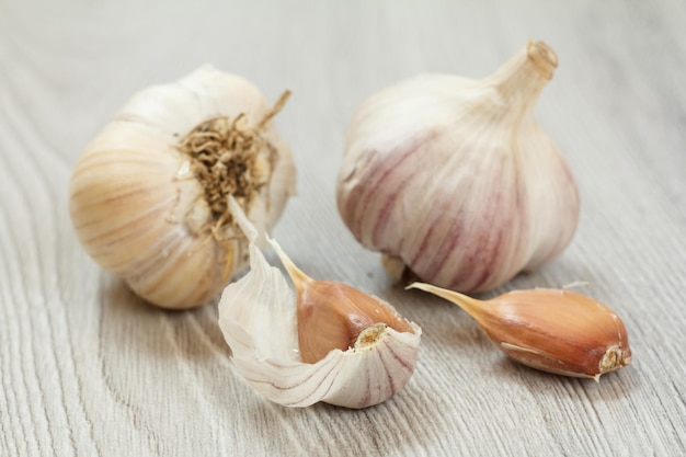 Vue rapprochée des bulbes d'ail épluchés et non épluchés crus sur un fond de bois gris