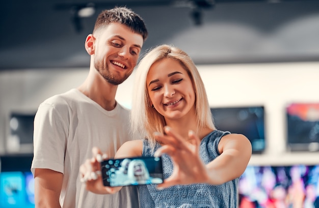 Vue rapprochée d'un charmant couple d'amoureux embrassant un jeune étudiant prenant un selfie avec un nouveau mobile dans un magasin de technologie.