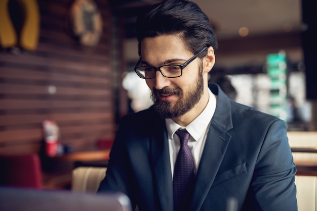 Vue rapprochée de concentré professionnel réussi jeune homme barbu en costume travaillant dans un café.