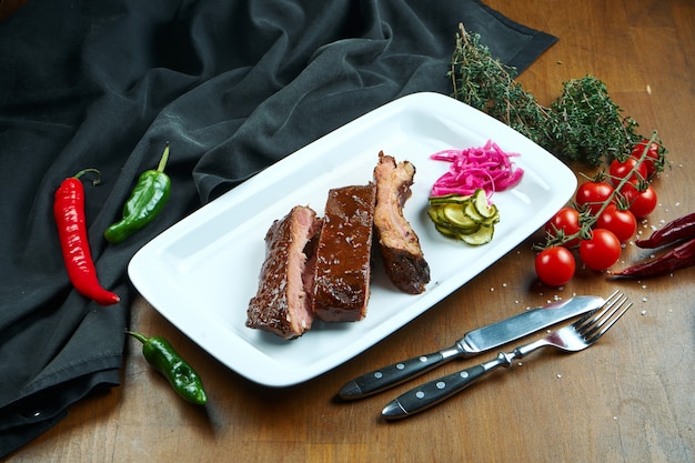 Vue rapprochée sur de délicieuses côtes de porc au four. Côtes levées barbecue - un plat classique de la cuisine américaine sur une plaque blanche.