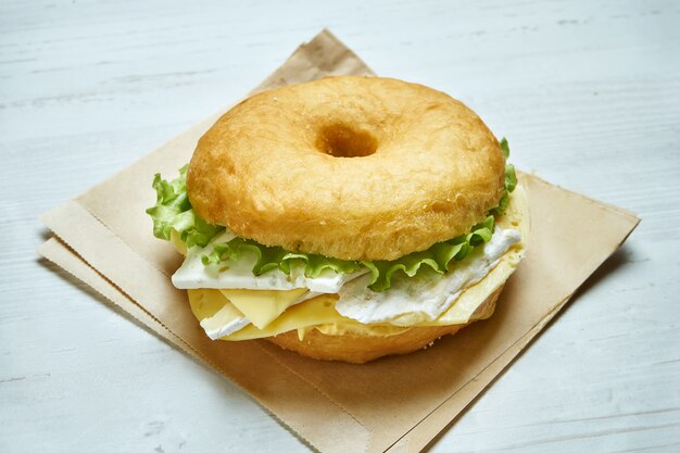 Vue rapprochée sur un délicieux bagel avec 4 types de fromage et de laitue sur une table en bois. Sandwich inhabituel aux beignets.