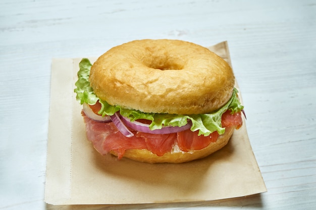 Vue rapprochée sur un délicieux bagel à l'oignon, à la feta et au saumon sur une table en bois. Sandwich inhabituel aux beignets. Nourriture du petit déjeuner