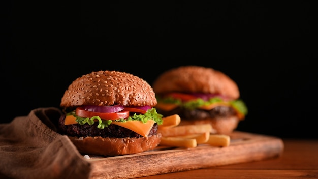 Vue rapprochée de délicieux hamburgers de boeuf grillé servis sur un plateau en bois sur la table avec mur noir