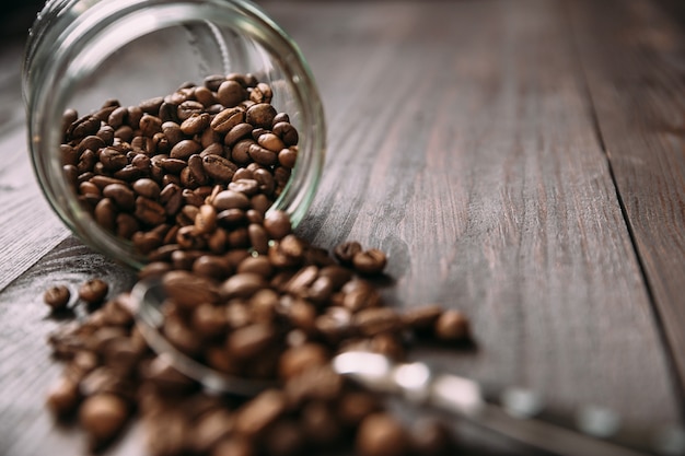 Vue rapprochée du bocal en verre avec des grains de café renversés sur une table en bois