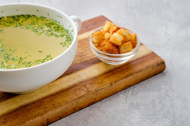 Vue rapprochée du bouillon de poulet avec des croûtons sur une planche de service en bois