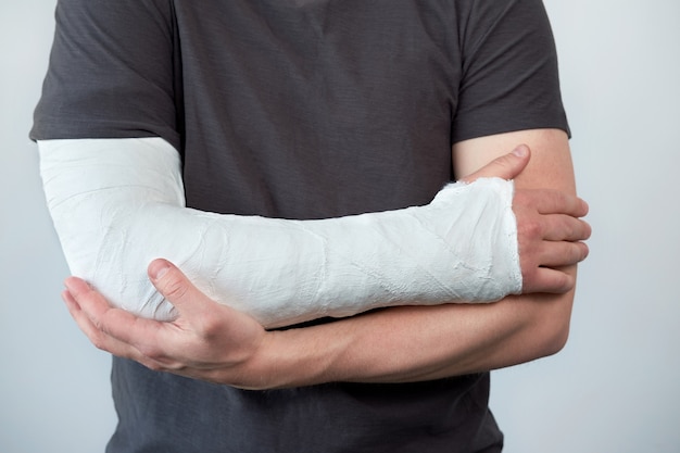 Vue rapprochée du bras de l'homme avec du plâtre sur un mur blanc