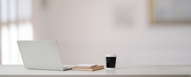 Vue rapprochée du bureau à domicile avec ordinateur portable, livres, tasse à café et espace copie sur tableau blanc