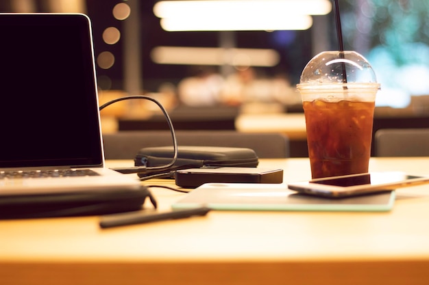 Photo vue rapprochée du café glacé dans une tasse jetable par ordinateur portable à la table