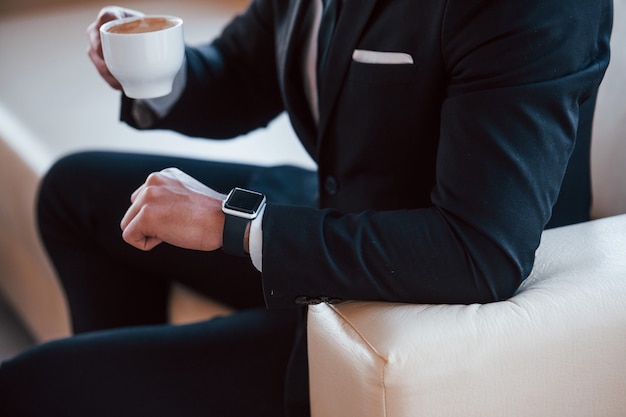 Vue Rapprochée Du Jeune Homme D'affaires En Costume Noir Et Cravate Avec Tasse F Verre Vérifier L'heure.