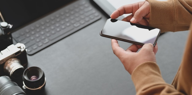 Vue rapprochée du photographe professionnel touchant un smartphone dans un lieu de travail élégant et sombre