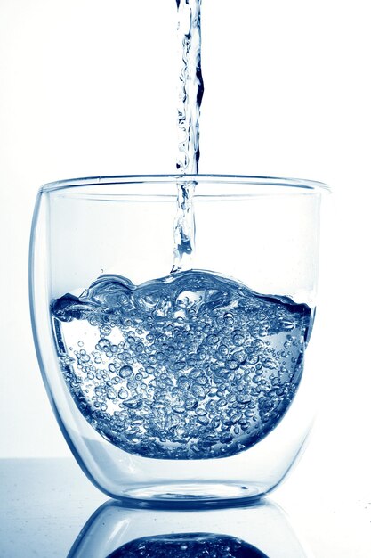 Photo vue rapprochée de l'eau qui coule dans le verre sur un fond blanc