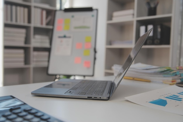 Vue rapprochée d'un espace de travail simple avec des cahiers d'ordinateur portable, une tasse de café et un pot d'arbre sur une table blanche avec un arrière-plan flou de la salle de bureau