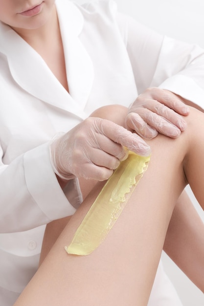 Vue rapprochée de l'esthéticienne enlevant les cheveux sur la jambe féminine à l'aide de cire chaude dans un salon de beauté professionnel