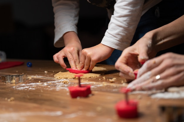 Vue rapprochée à faible angle d'un enfant faisant des biscuits faits maison avec sa mère sur une table à manger en bois.