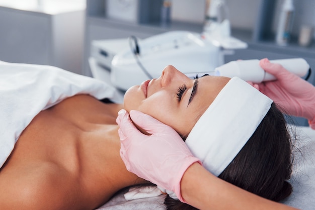 Vue rapprochée d'une femme allongée dans un salon de spa et ayant une procédure de nettoyage du visage à l'aide d'un appareil moderne.