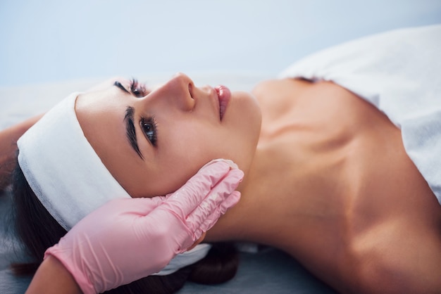 Vue rapprochée d'une femme allongée dans un salon de spa et ayant une procédure de nettoyage du visage par un cosmétologue en gants.