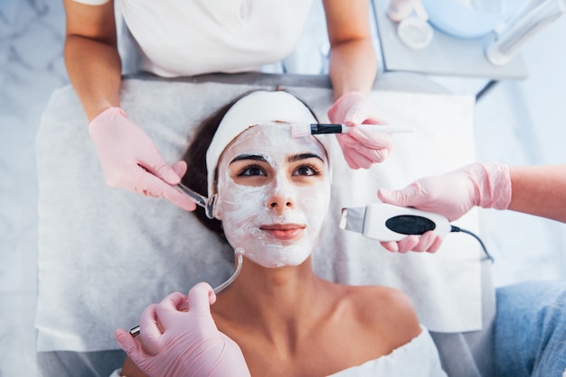 Vue rapprochée d'une femme allongée dans un salon de spa et ayant une procédure de nettoyage du visage par différents appareils et masques.