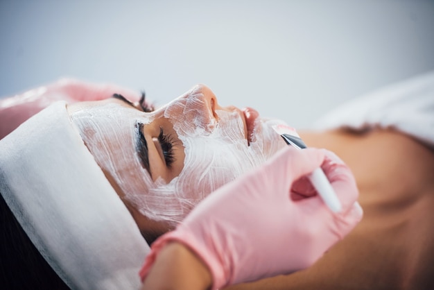 Vue rapprochée d'une femme allongée dans un salon de spa et ayant une procédure de nettoyage du visage par le masque.