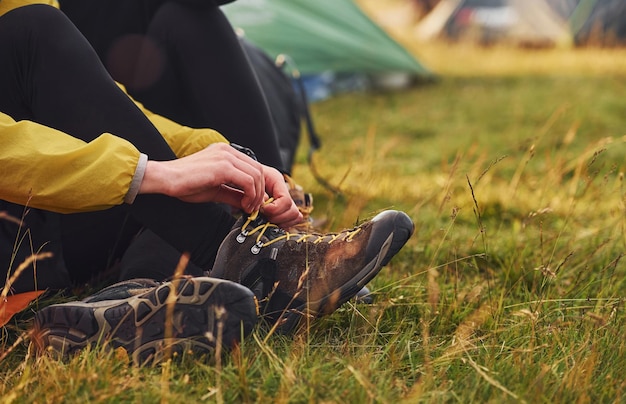 Vue rapprochée de la femme assise près de la tente et portant des chaussures à l'extérieur sur le pré
