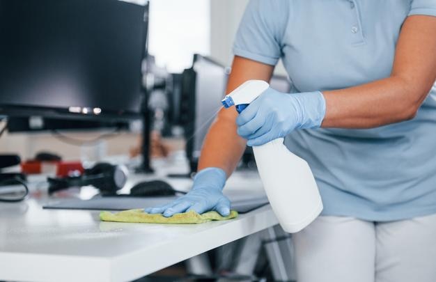 Vue rapprochée de la femme dans des gants de protection qui nettoient les tables au bureau