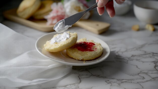 Vue rapprochée d'une femme mettant la crème coagulée et la confiture sur scone