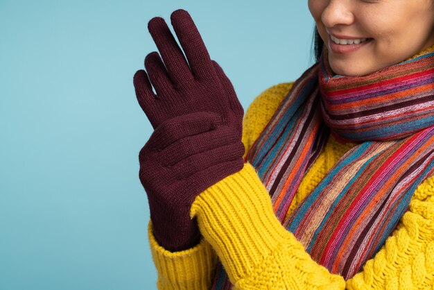 Photo vue rapprochée de la femme en pull jaune élégant mettant ses gants. fille cool en écharpe tricotée chaude et gants posant sur fond bleu. concept d'hiver