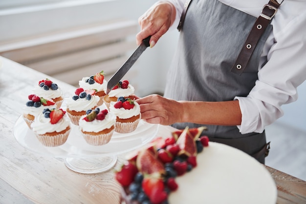 Photo vue rapprochée d'une femme qui fait des tranches de biscuits à l'aide d'un couteau dans la cuisine avec une tarte sur la table.