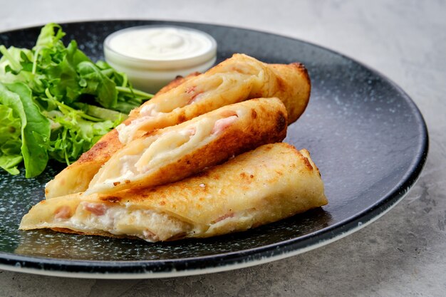 Vue rapprochée d'une fine crêpe farcie de fromage fondu et de jambon sur une assiette