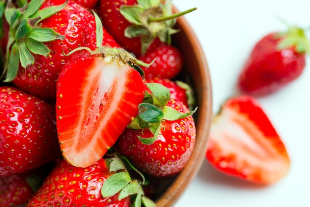 Vue rapprochée de fraises biologiques mûres fraîchement cueillies dans un bol en bois sur une surface blanche