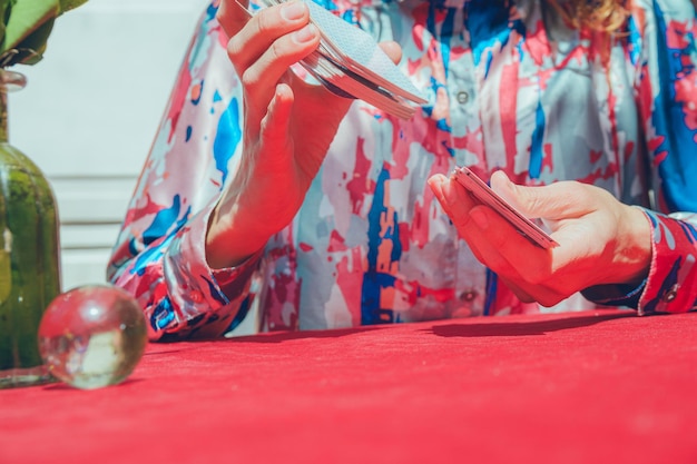 Vue rapprochée et frontale d'une femme caucasienne méconnaissable assise à mélanger des cartes de tarot sur une table avec une nappe rouge.