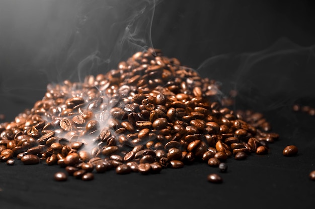 Vue rapprochée de grains de café fraîchement torréfiés avec de la fumée en arrière-plan