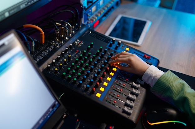 Vue rapprochée d'en haut de la piste de mixage à la main de l'ingénieur du son sur le panneau de commande du mélangeur de son à la maison de production