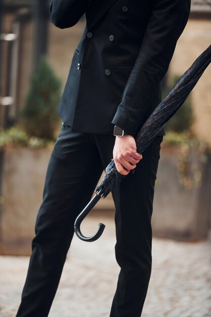 Vue rapprochée Holding parapluie Jeune homme élégant dans des vêtements chics formels à l'extérieur de la ville